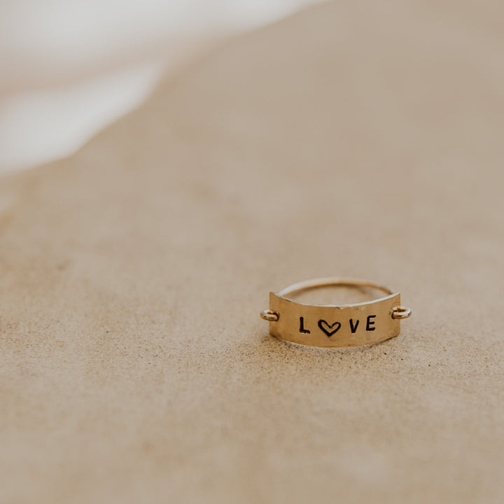 Gold ring with 'LOVE' engraving on a sandy surface