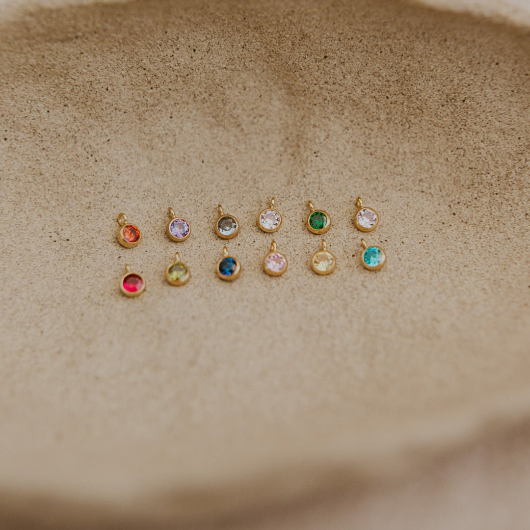 Set of small gold earrings with colored gemstones on a textured beige surface