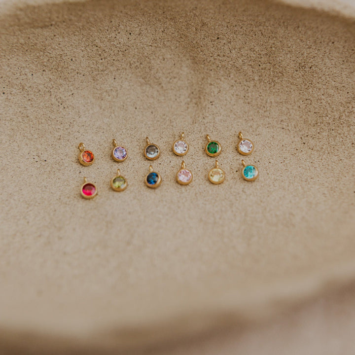 Set of small gold earrings with colored gemstones on a textured beige surface