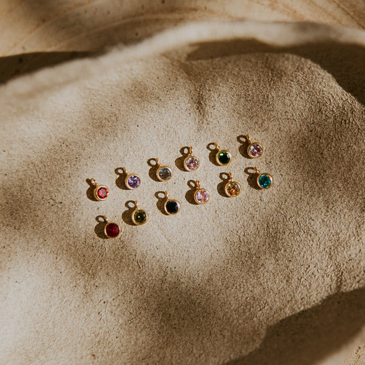 Small jewelry charms with colorful gemstones on a textured surface
