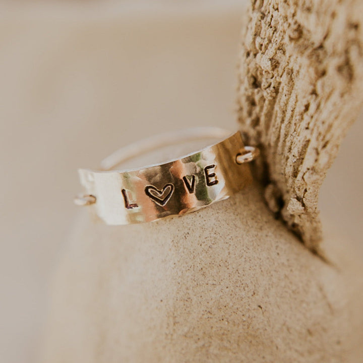 Gold ring with 'I ❤️ V E' text on a stone surface