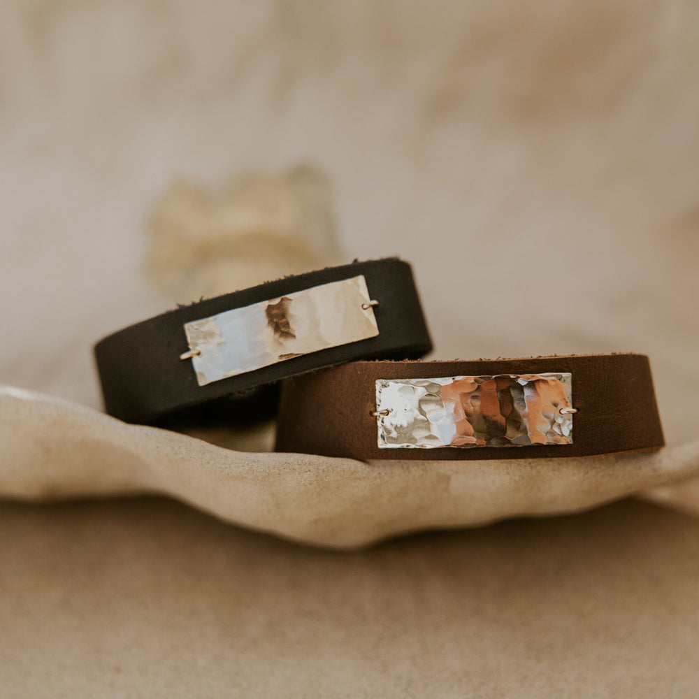 Two brown leather bracelets with embedded stones on a beige fabric background