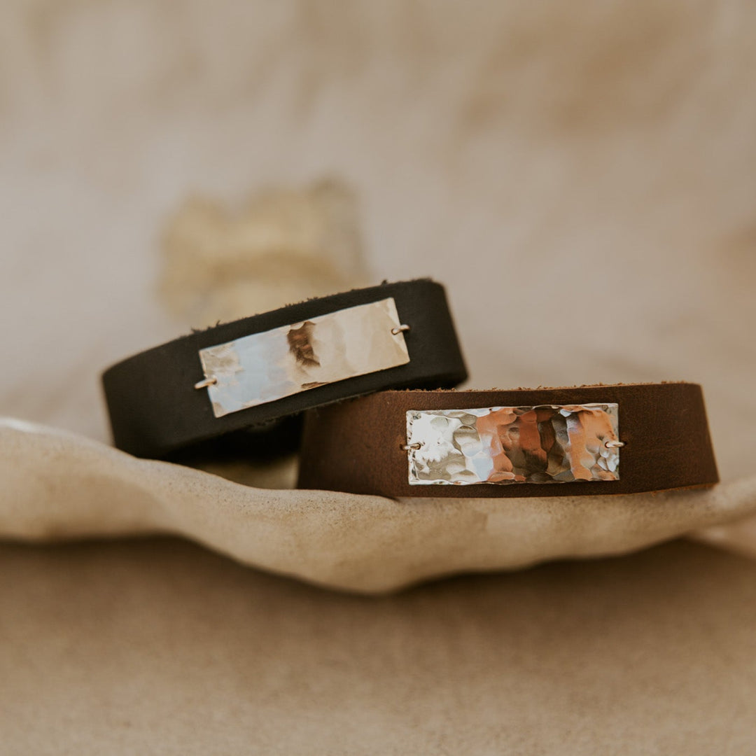 Two brown leather bracelets with embedded stones on a beige fabric background