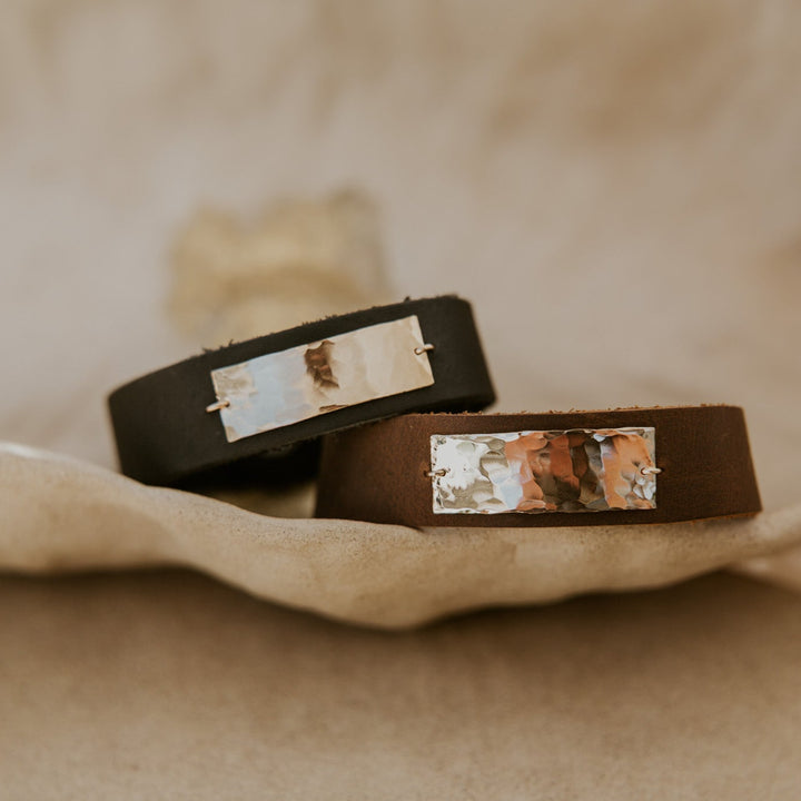 Two brown leather bracelets with embedded stones on a beige fabric background