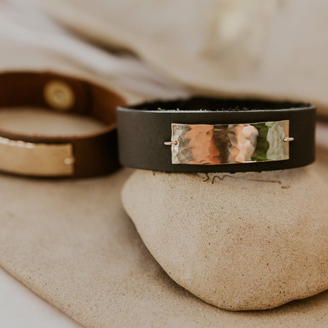 Two leather bracelets with metal accents on a stone surface