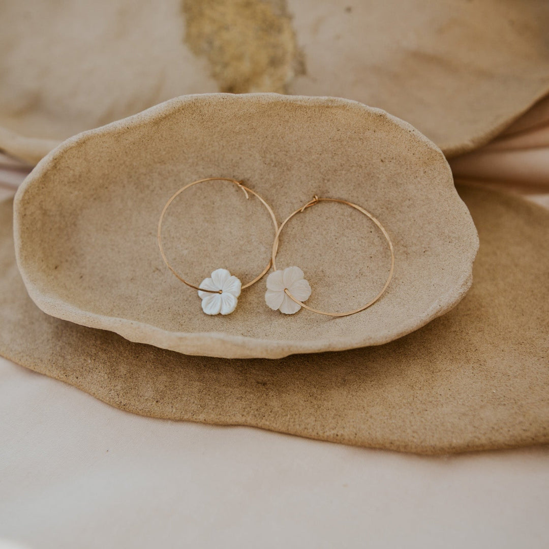 Pair of gold hoop earrings with floral details on a beige ceramic dish.