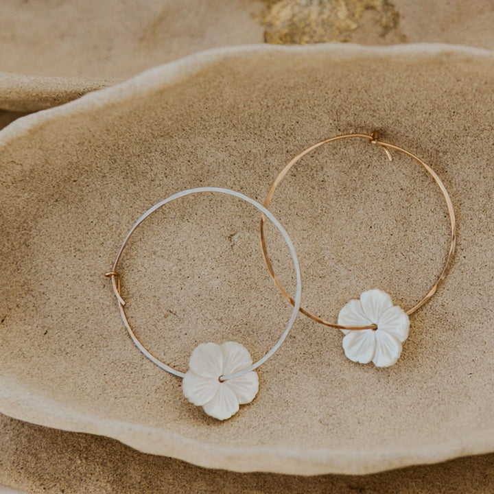 Gold hoop earrings with floral charms on a stone surface