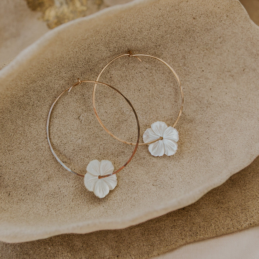 Gold hoop earrings with floral details on a stone surface