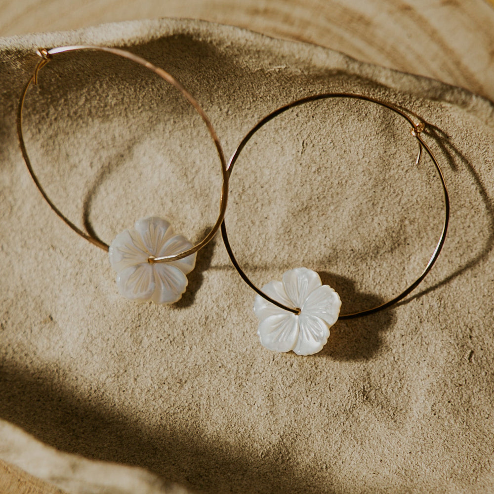 Gold hoop earrings with floral charms on a wooden surface