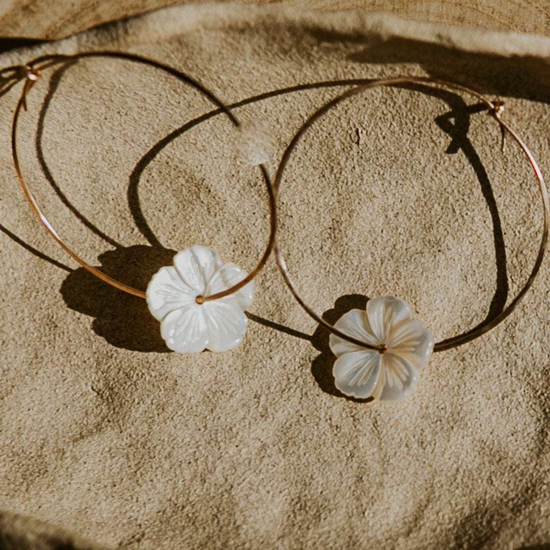 Gold hoop earrings with floral charms on a stone surface
