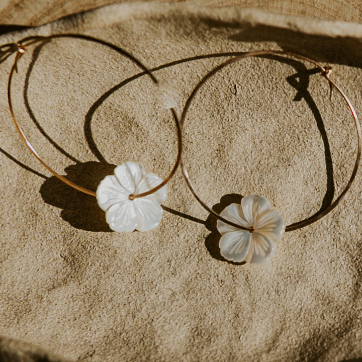 Gold hoop earrings with floral charms on a stone surface