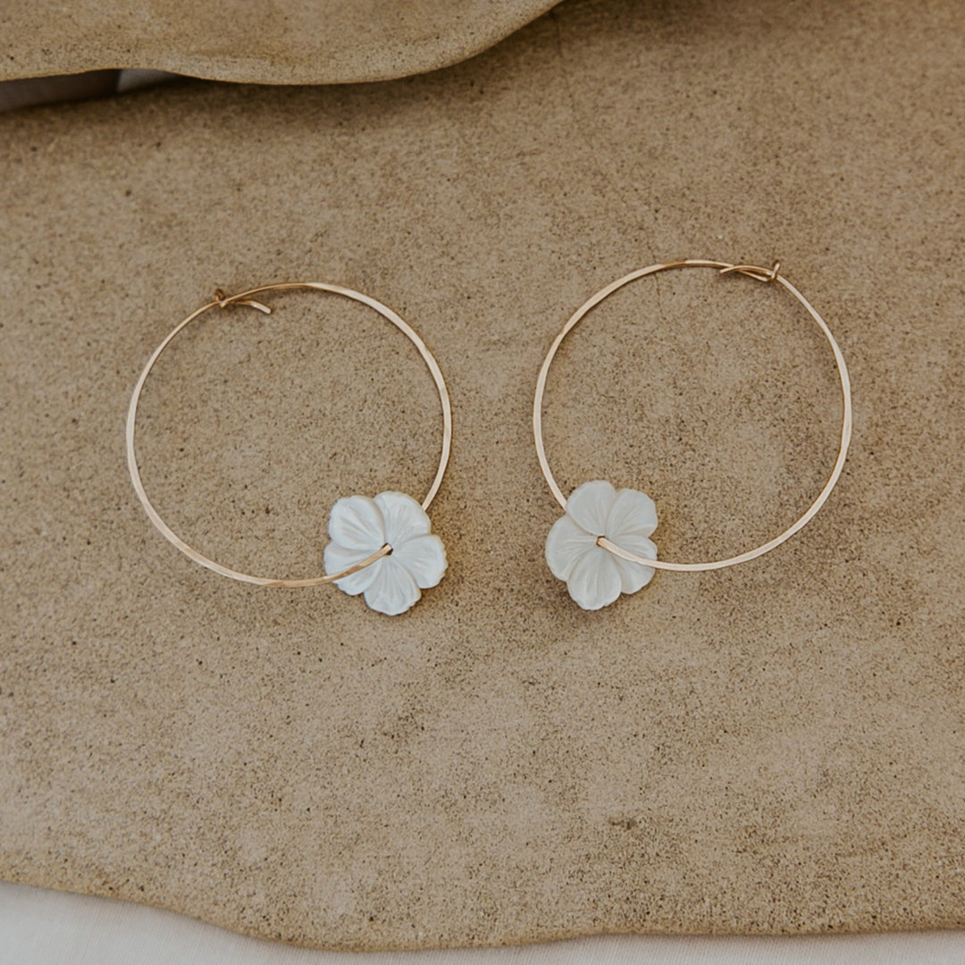 Pair of gold hoop earrings with leaf-shaped charms on a beige surface