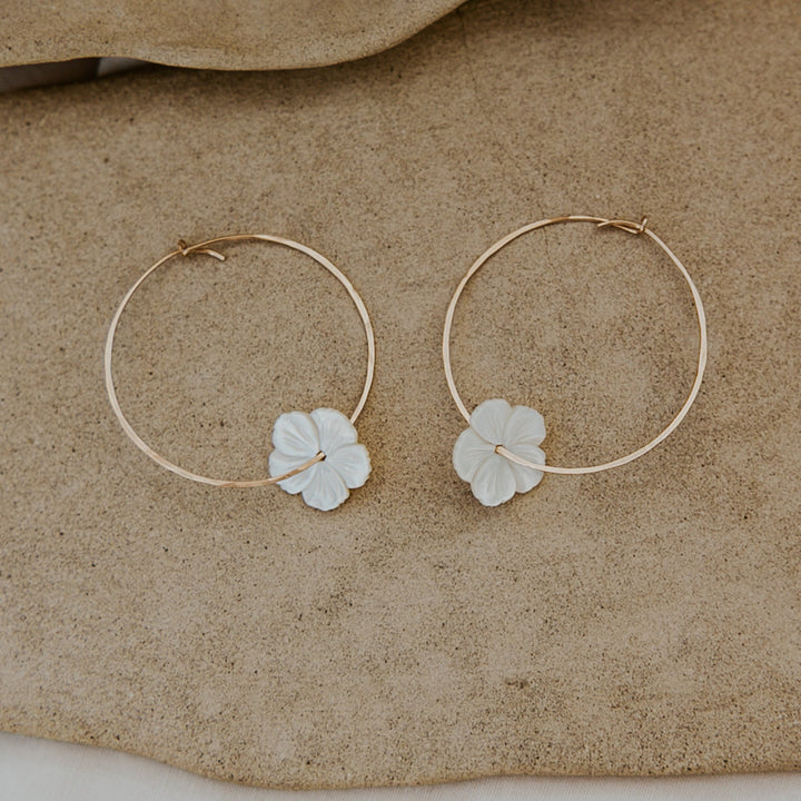 Pair of gold hoop earrings with leaf-shaped charms on a beige surface