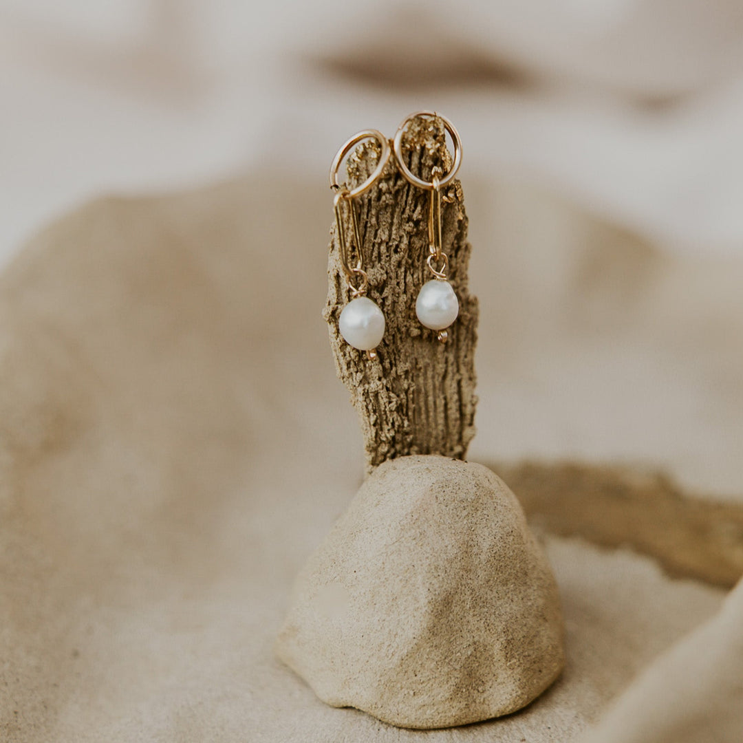 Gold earrings with pearl-like beads on a textured surface