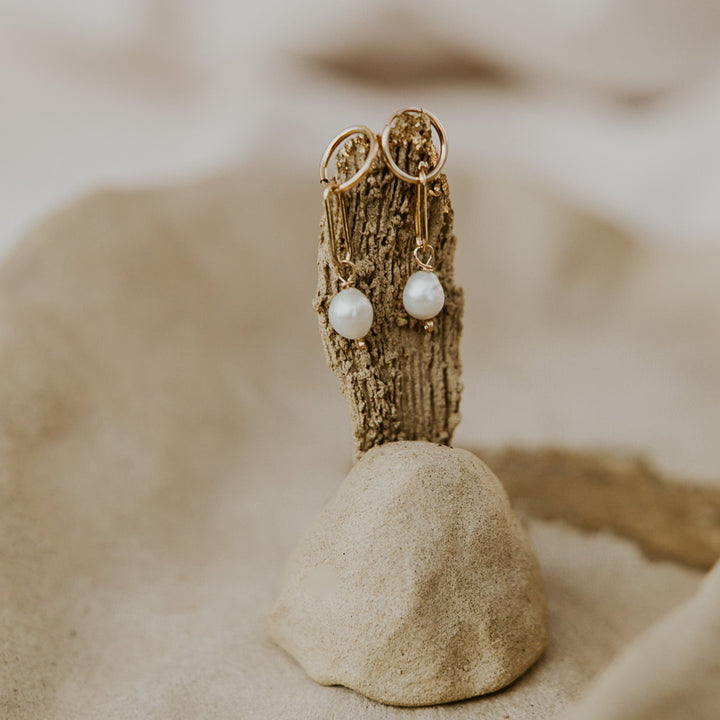Gold earrings with pearl-like beads on a textured surface