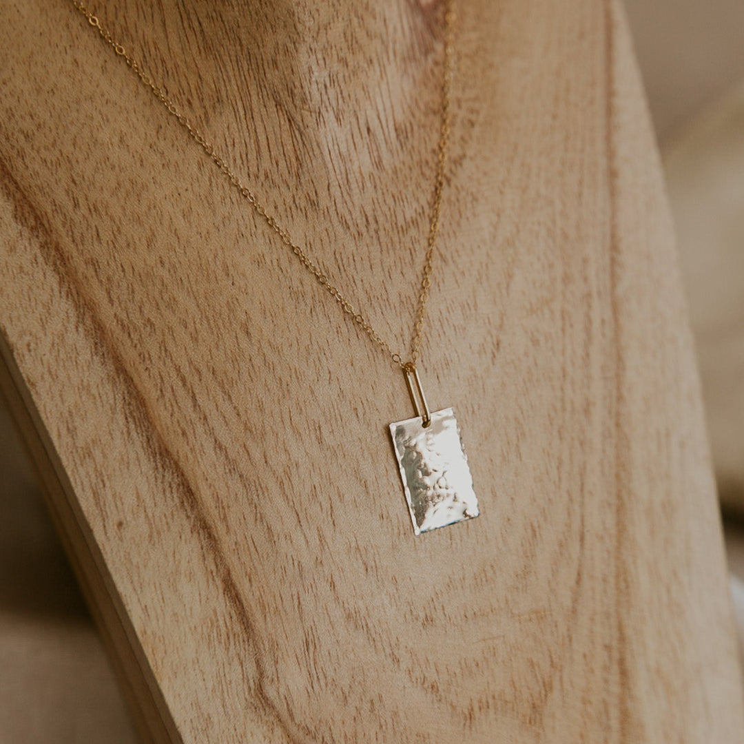 Gold necklace with a rectangular pendant on a wooden surface