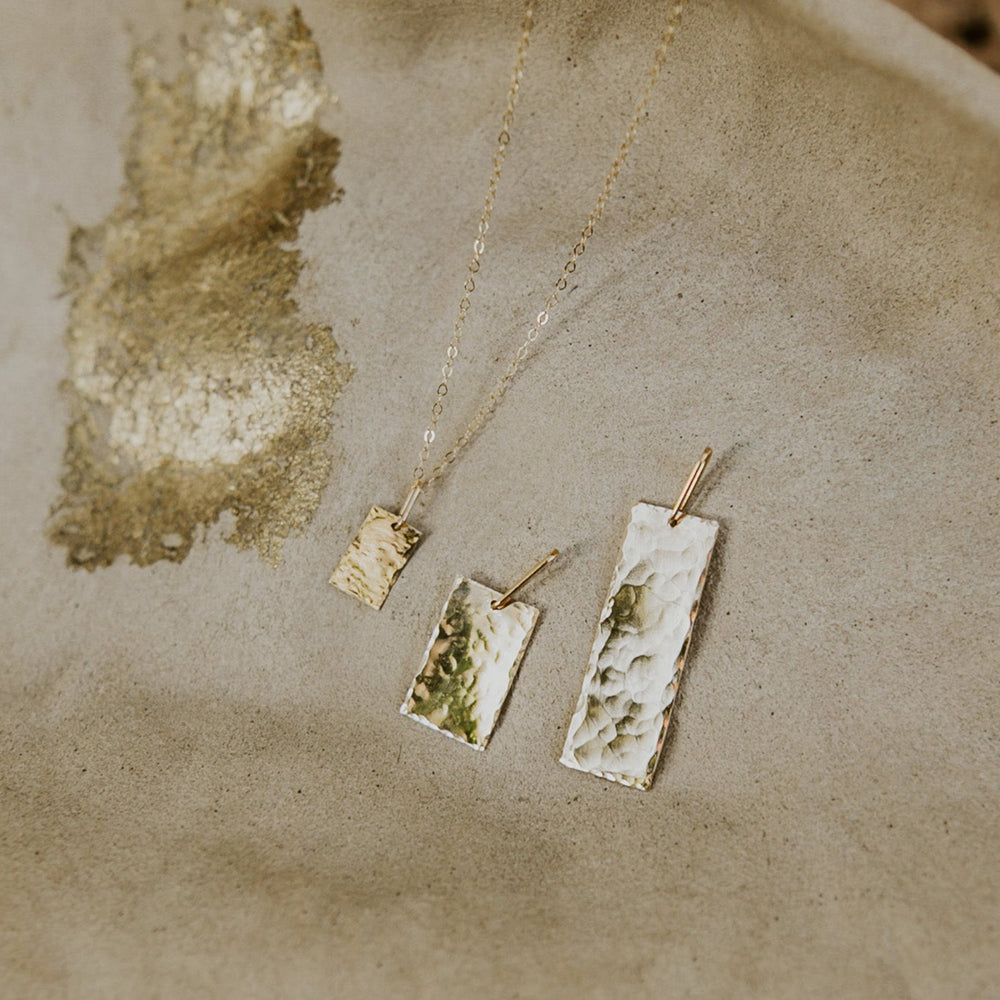 Gold necklace with three pendant tags on a textured beige surface