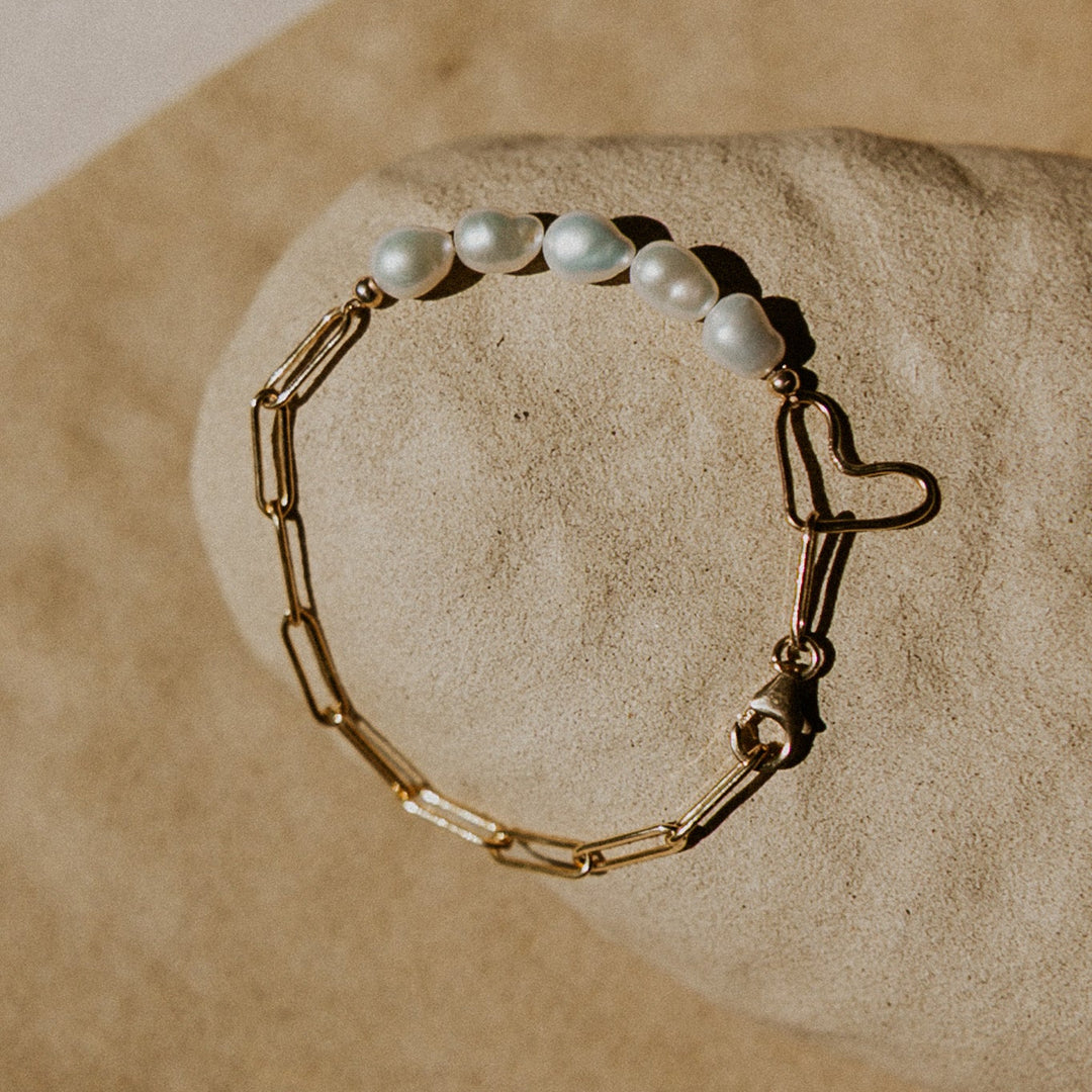 Gold chain bracelet with pearl beads on a beige stone surface