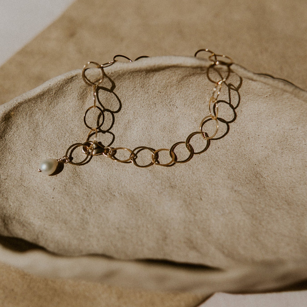 Gold bracelet with a pearl on a beige stone surface