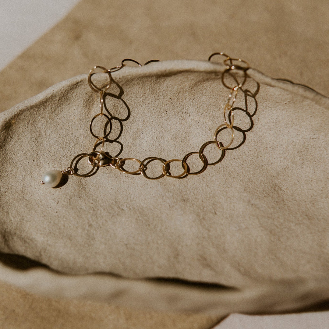 Gold bracelet with a pearl on a beige stone surface