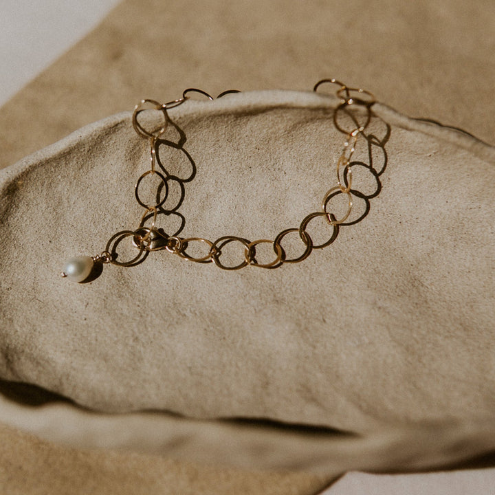 Gold bracelet with a pearl on a beige stone surface