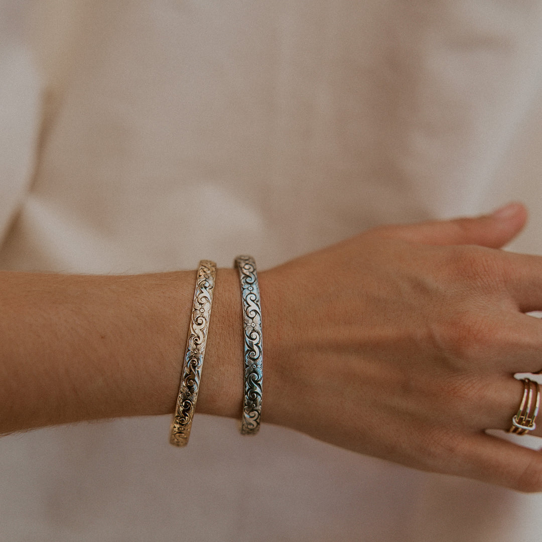 Close-up of a wrist wearing two ornate bracelets on a neutral background