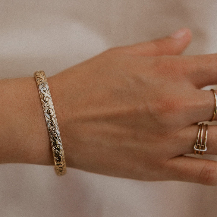 Hand wearing a gold bracelet and rings on a plain background