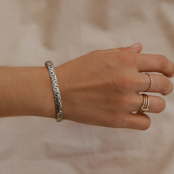 Hand wearing a silver bracelet and gold rings on a neutral background