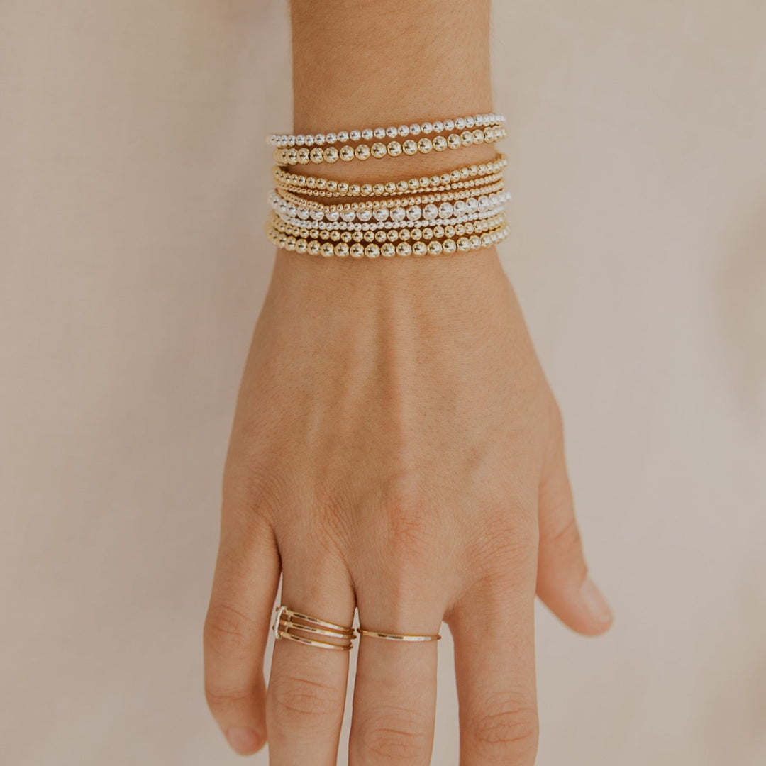 Hand wearing multiple mixed metal beaded bracelets on a beige background