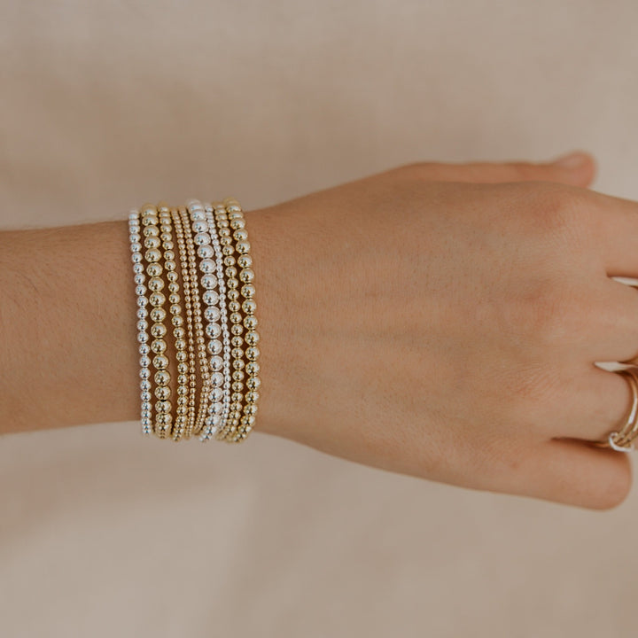 Hand wearing multiple pearl bracelets on a neutral background