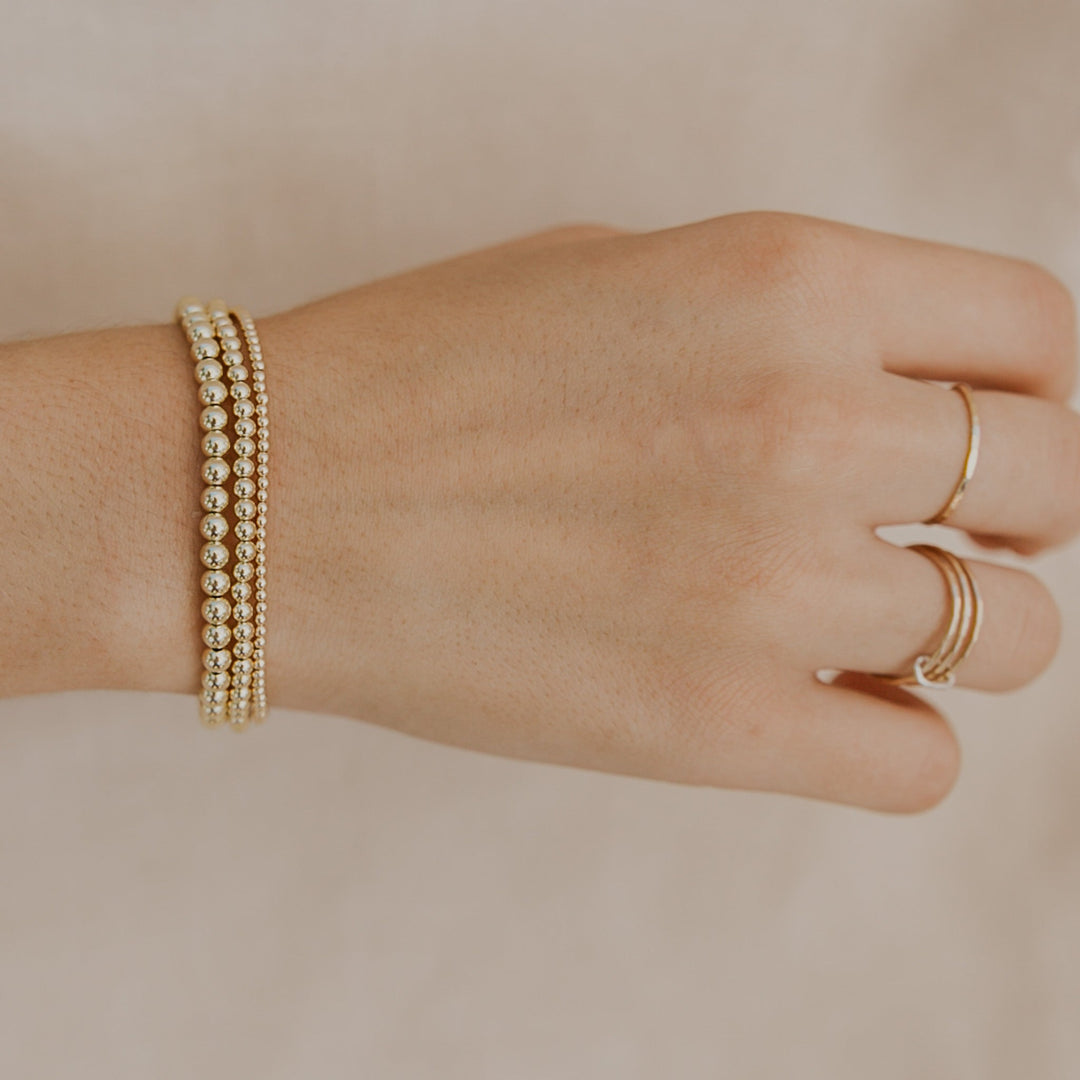 Hand wearing a gold bracelet and ring on a beige background