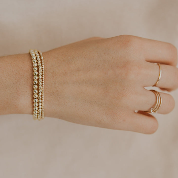 Hand wearing a gold bracelet and ring on a beige background