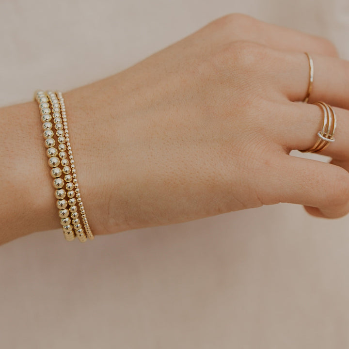 Hand wearing a gold bracelet and multiple rings on a neutral background