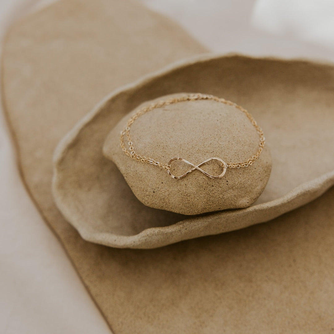Gold bracelet with an infinity symbol on a textured beige surface