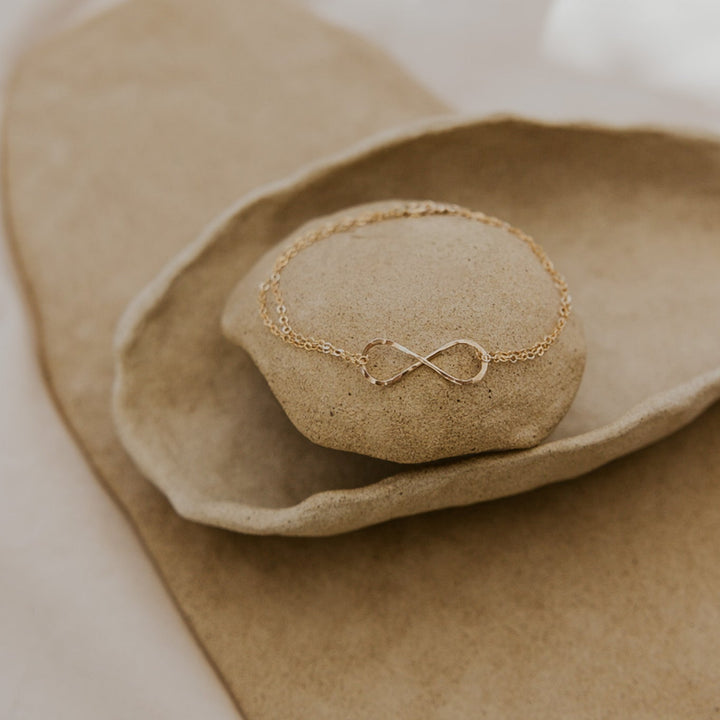 Gold bracelet with an infinity symbol on a textured beige surface