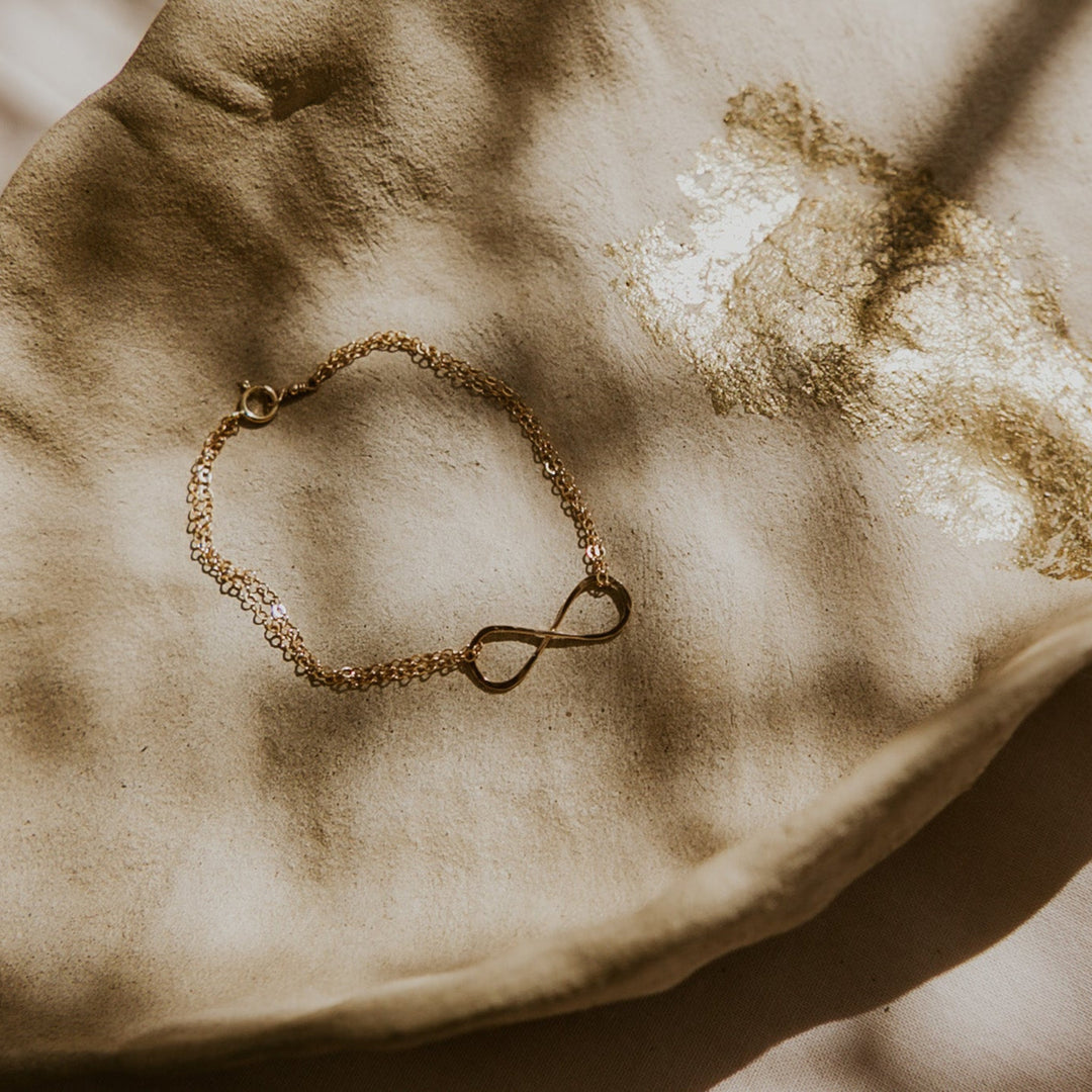 Gold bracelet with an infinity symbol on a textured beige surface