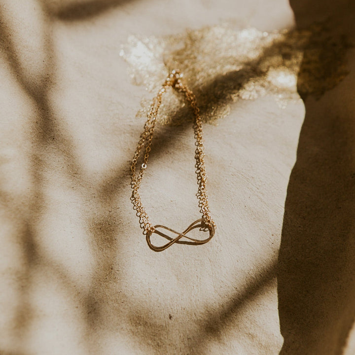Gold infinity necklace on a textured surface with a blurred background