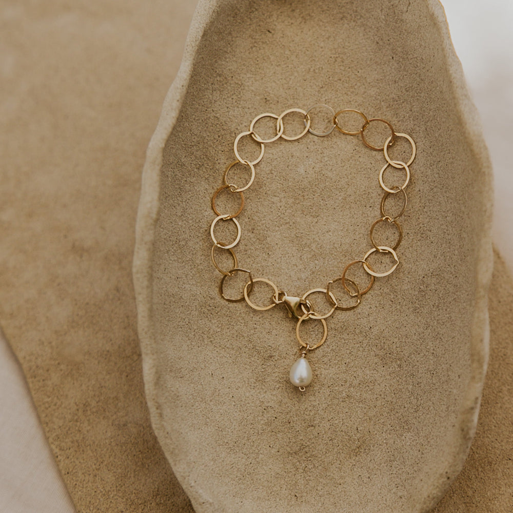 Gold chain bracelet with a pearl pendant on a stone surface