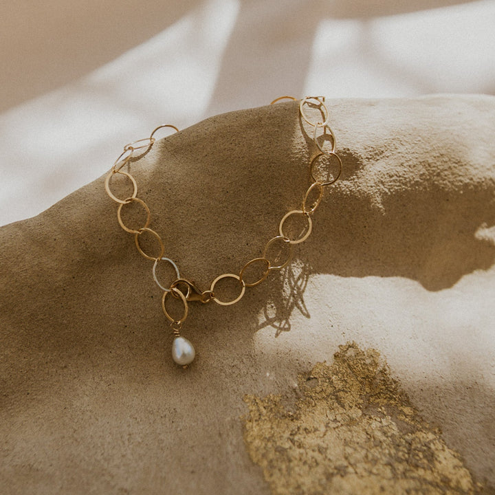 Gold bracelet with a pearl charm on a textured surface