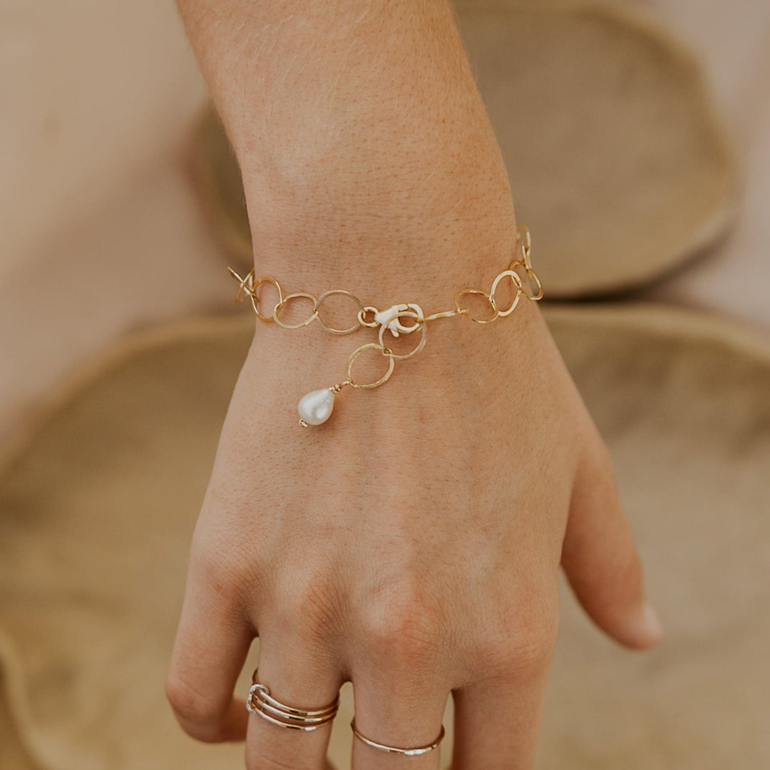 Gold bracelet with a pearl charm on a wrist against a neutral background