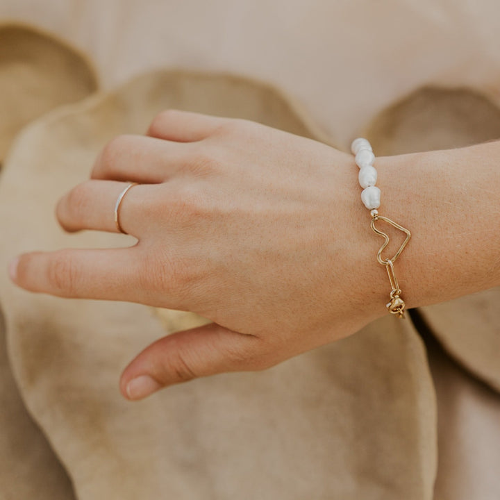 Hand wearing a gold bracelet with white beads on a blurred background