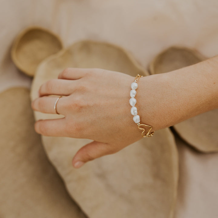Hand wearing a pearl bracelet with a heart charm on a beige background
