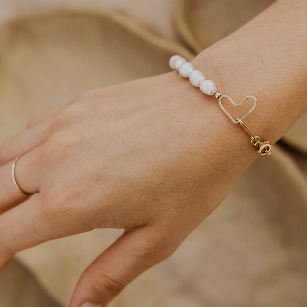 Hand wearing a pearl bracelet with a heart charm on a blurred beige background