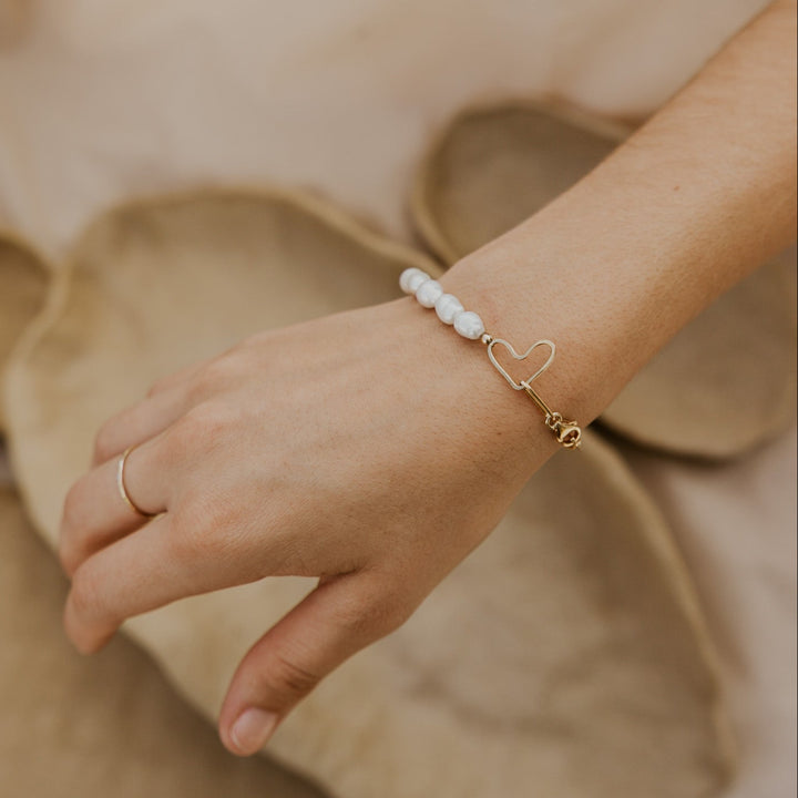 Hand wearing a ring and bracelet on a soft beige background