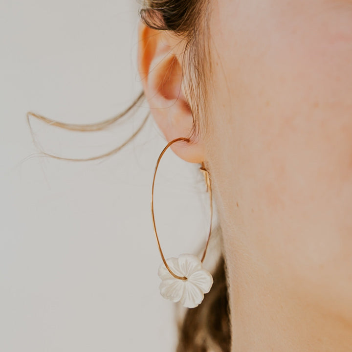 Close-up of a gold hoop earring with a floral charm worn by a person.
