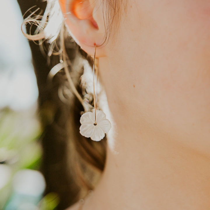 Close-up of a person wearing a delicate flower-shaped earring with a blurred natural background