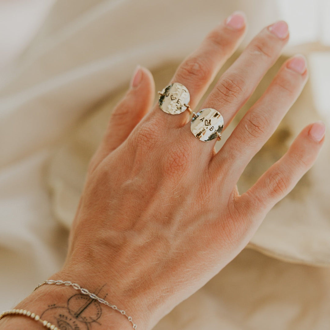 Hand wearing two gold rings on a neutral background