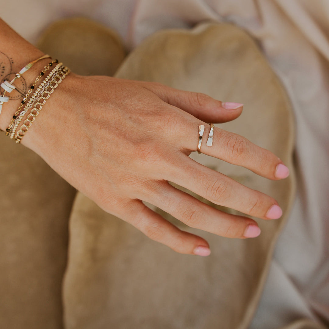 Hand wearing a gold ring with multiple bracelets on a neutral background
