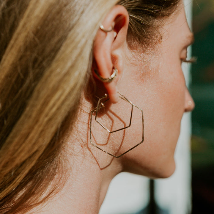 Close-up of a person wearing gold hoop earrings with a blurred background