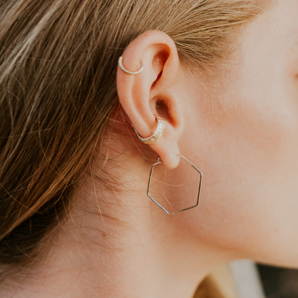 Close-up of an ear wearing two gold hoop earrings with a blurred background